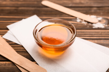 Glass bowl with sugaring paste, wax strips and sticks on wooden background