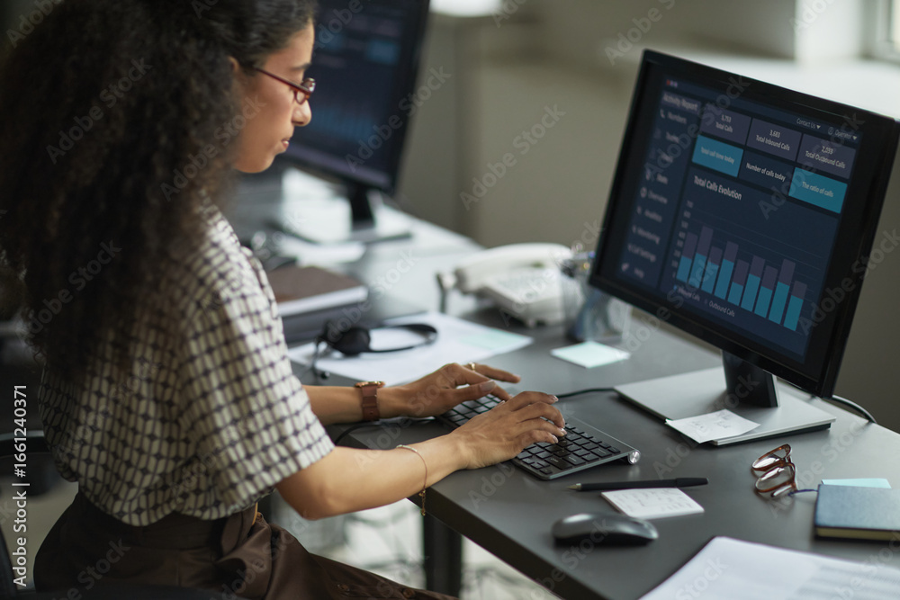 Wall mural young adult woman working at desk using desktop computer with data analytics dashboard on screen, ty