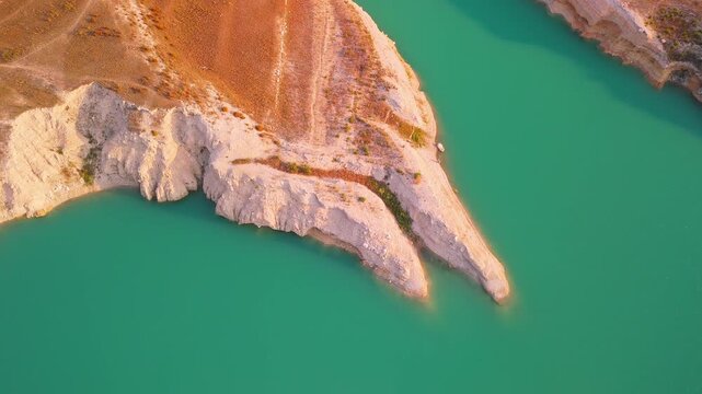 Drone video captures a rocky shoreline with green vegetation surrounded by bright turquoise waters of a lake in Spain, viewed directly from above.