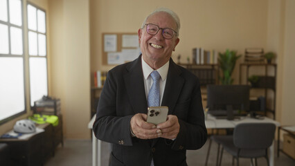 Senior man in suit smiling while using smartphone in modern office interior, showcasing a professional and confident demeanor amidst a business setting with contemporary decor.