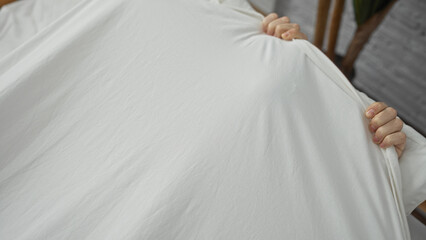 Young man grasping bedsheet tightly in a cozy bedroom setting showcasing minimalistic interior and...