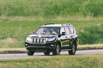 Fototapeta premium Body on frame truck driving along an asphalt road, surrounded by lush green grass and towering trees