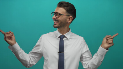 Man in white shirt pointing fingers wearing glasses and tie in a turquoise studio; confidence direction.