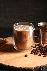 Glass cup of iced latte with coffee beans and cezve on black background