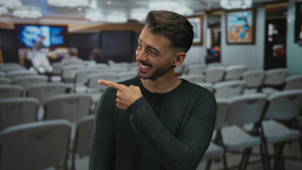 Man wearing green sweater points finger at framed painting inside building with smile; curiosity...