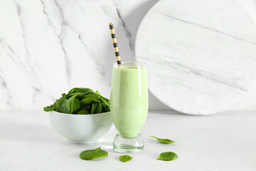 Glass of fresh smoothie and bowl with spinach on white background