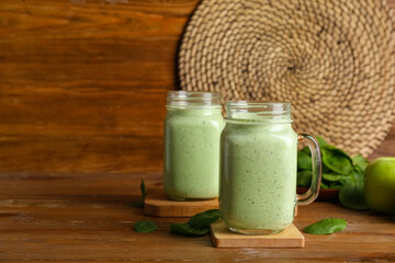 Mason jars of fresh spinach smoothie on wooden background