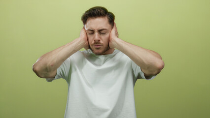Young man with beard isolated against yellow background covering ears with hands in expression of...