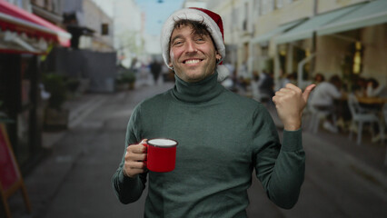 Hispanic man wearing christmas hat smiling holds red cup while pointing on busy street suggesting a festive mood outdoors.
