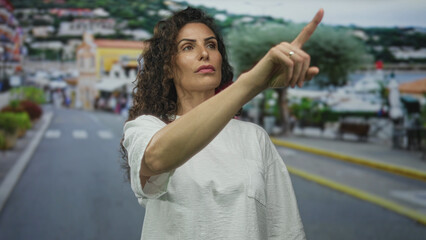 Hispanic woman pointing finger at building facade on urban street; determination confidence ambition resilience.