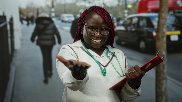 Smiling woman doctor extending hand on city street with clipboard in urban outdoor setting showing friendly gesture to camera during daytime