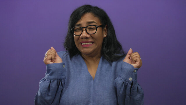 African american woman in casual blue shirt shrugging shoulders in purple studio with palms up gesture expressing puzzled doubt; confusion.