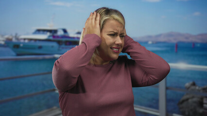 Woman covers ears at a busy port boat dock by a white yacht against metal railing with strained...