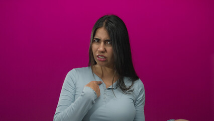 Young hispanic woman pointing her index finger with a dismissive gesture in an isolated pink studio...