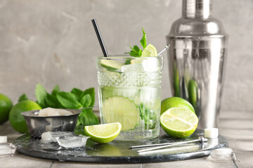 Glass of fresh Mojito cocktail with limes and shaker on grey tile table