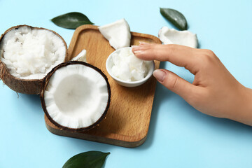 Female hand, wooden tray and coconut oil on blue background, closeup