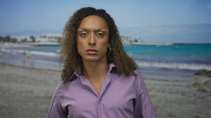 Woman face gazing at camera with slight head tilt in purple shirt on beach; self acceptance serenity.