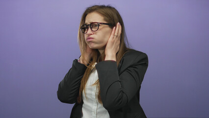 Young caucasian woman in white shirt and black blazer covers her ears and winces in a studio scene;...