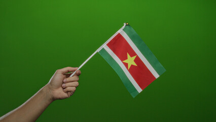 Hand holding suriname flag against a vibrant green wall showcasing patriotic pride and cultural...
