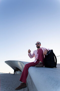 Stylish person sitting outdoors at MAAT Lisbon with sunglasses and backpack