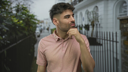 Man in pink polo shirt shrugs shoulders on city street lined with black iron railings and lush...