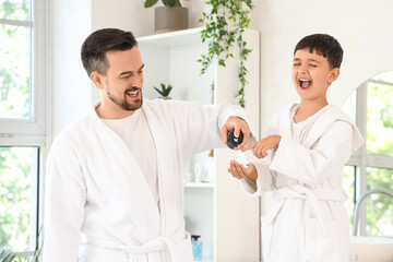 Happy father and his little son with bottle of shaving foam in bathroom