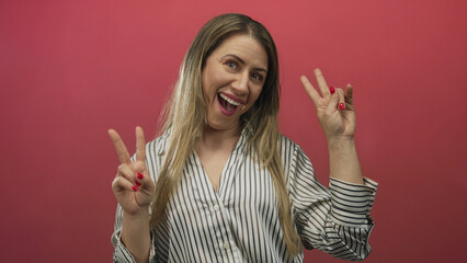 Blonde middle age woman smiling showing two hands peace sign gesture in studio with red wall;...