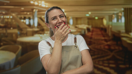 Woman covers mouth with hand in building interior near table under warm lighting; joy spontaneity.