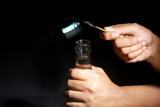 Female hand opening bottle using metal opener with isolated black background