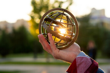 Hand holding armillary sphere capturing bright sunset in park. Astrological Sign. Zodiac