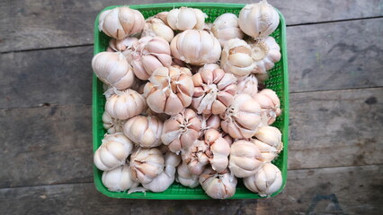Top view of a green basket filled with tied garlic bulbs, placed on a rustic wooden surface, ready for cooking or sale.
