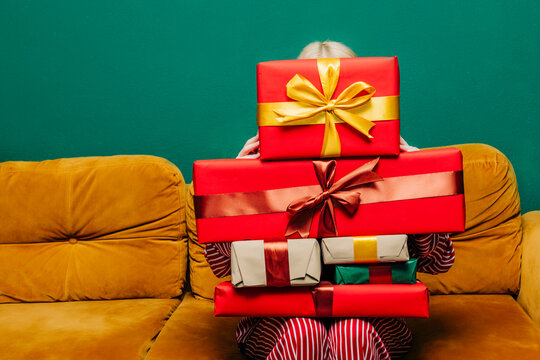 Person in red pajamas sitting on sofa with stack of Christmas gifts