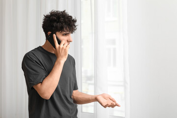 Young man talking by mobile phone with mold on light wall near window at home