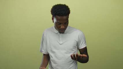 Young african american man looks down at bare hands in a green studio setting; serene introspection.