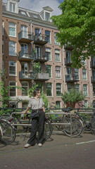 Obraz premium Woman enjoying sunny day by amsterdam canals, surrounded by bicycles and historic brick buildings, embodying vibrant city life and european charm.