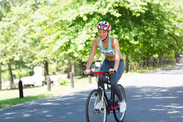 Asian woman riding black bicycle on park path wearing red-and-white helmet and bib number 452