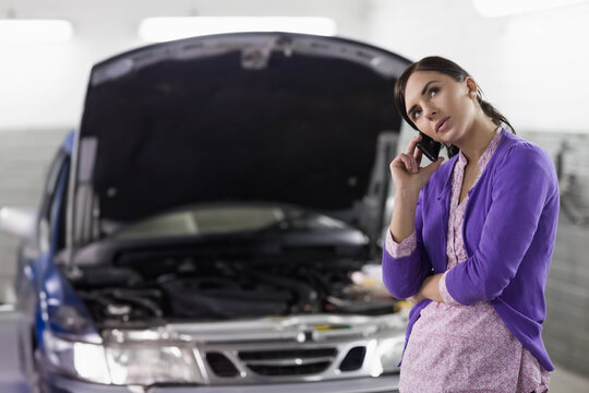 Adult female using smartphone beside silver sedan with engine components in garage, copy space