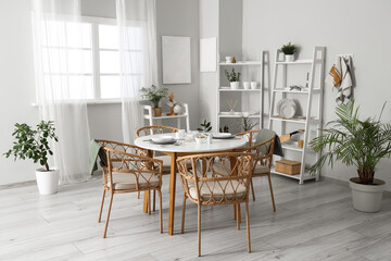 Served dining table with wicker chairs and shelving units in interior of stylish kitchen