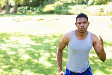 Fototapeta premium African American man running on grass in park wearing gray athletic shirt, blue shorts, copy space