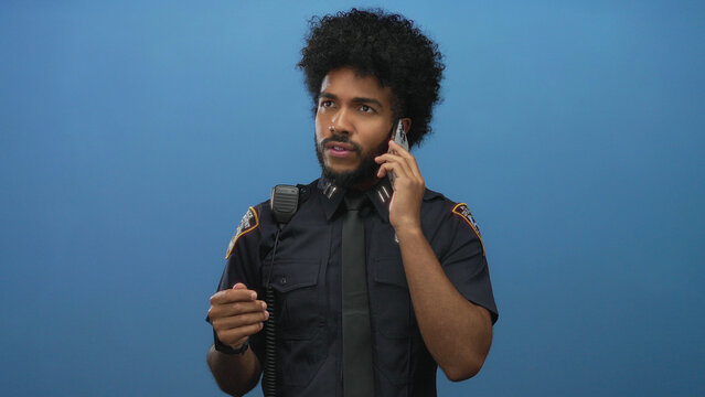 African american man in police uniform using smartphone against isolated blue wall background.