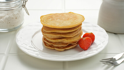 Stack of golden pancakes with strawberries on a white plate, breakfast food
