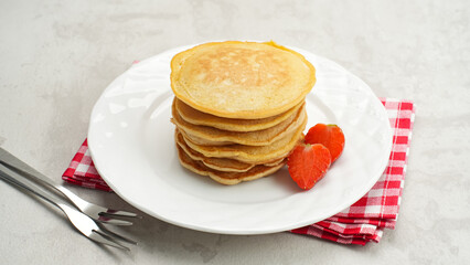 Stack of golden pancakes with strawberries on a white plate, breakfast food
