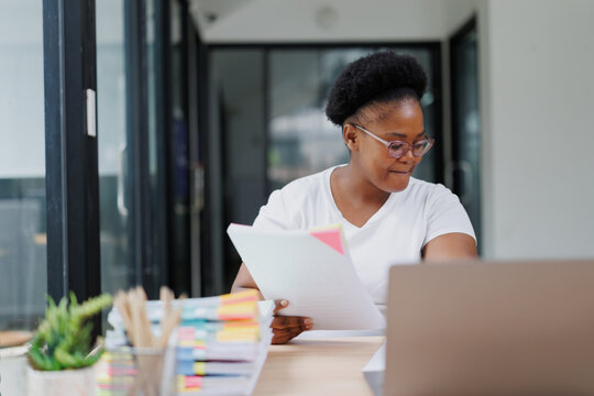 Young black businesswoman reviewing documents and working with her laptop, managing her business and finances in a bright and modern office space