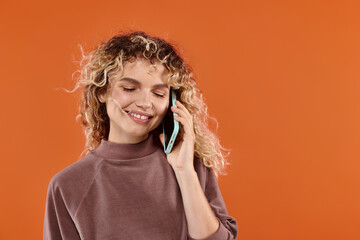 Radiant young woman enjoying a joyful conversation against a vibrant orange backdrop
