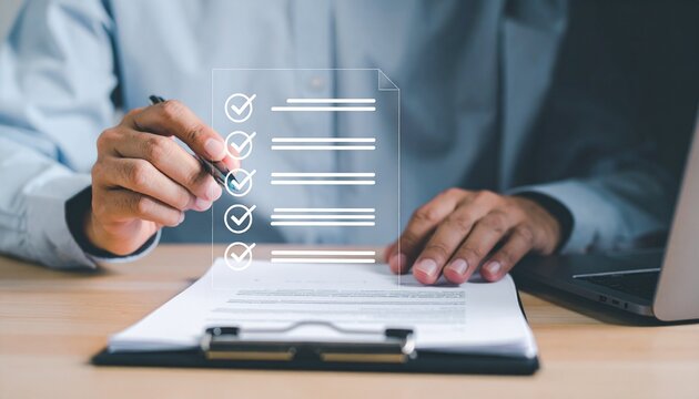 Hands writing on clipboard beside a laptop with checkmarks