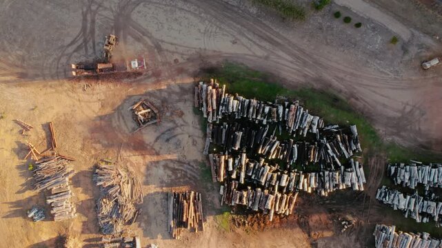 Aerial view of a heavy fork lifter offloading a truck with logs at lumber yard filled with stacked timber, and heavy machinery on a sunny afternoon