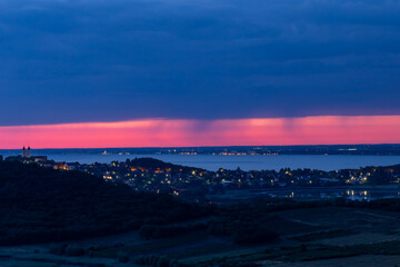 Scenic pre-dawn view from the Tihany lookout, showing the silhouette of the Tihany Abbey and Lake Balaton under a calm sky with a red stripe on the horizon.