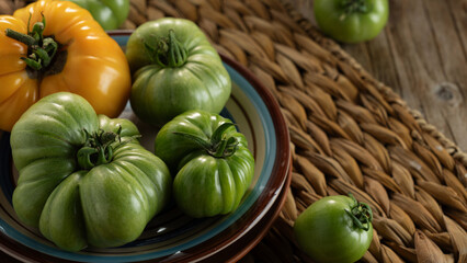 Freshly harvested green tomatoes displayed on a woven tray with a vibrant yellow tomato