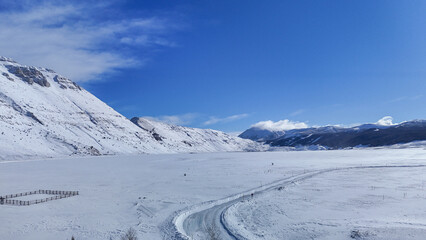 Winter landscape unfolds with majestic mountains, snowy plains, and a winding road under the bright...