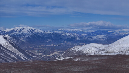 Fototapeta premium Snow-capped mountains rise majestically under a blue sky, showcasing a breathtaking winter vista in a serene valley